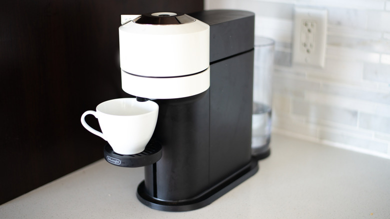 A Vertuo machine is on a counter with the brew button visible on top.