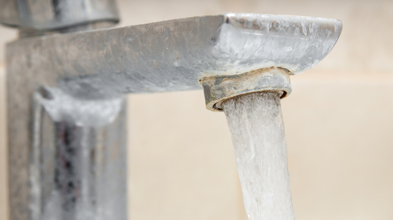 Water is flowing from a tap covered in limescale.