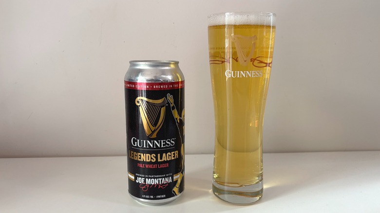 Can of Guinness Legends Lager next to pint glass of lager on white table
