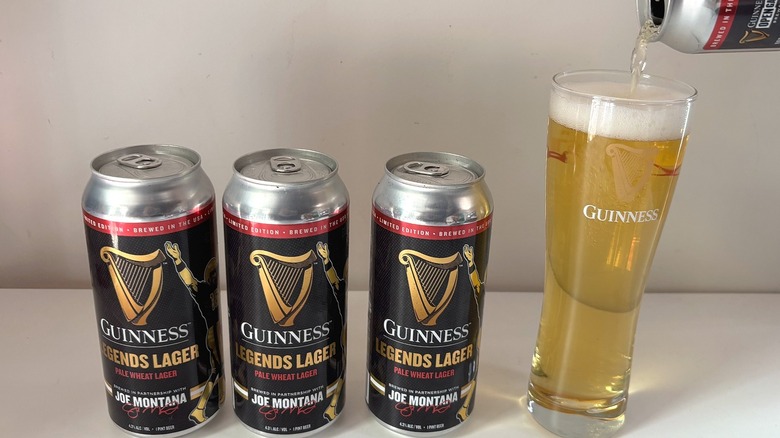 Pouring can of Guinness Legends Lager into pint glass, three cans beside