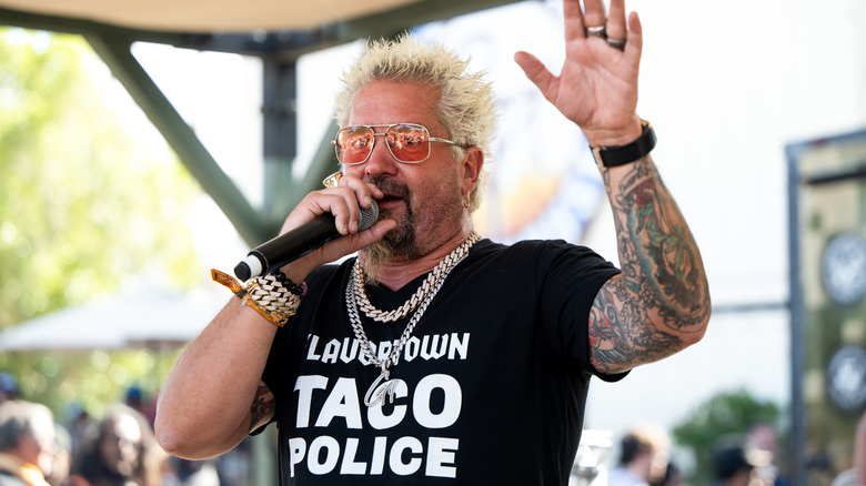 Guy Fieri speaking into a microphone while waving