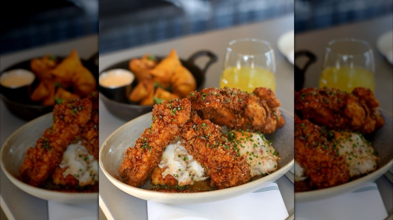 A bowl of chicken and biscuits in front of blurred restaurant table with side dish and drink, mirrored image