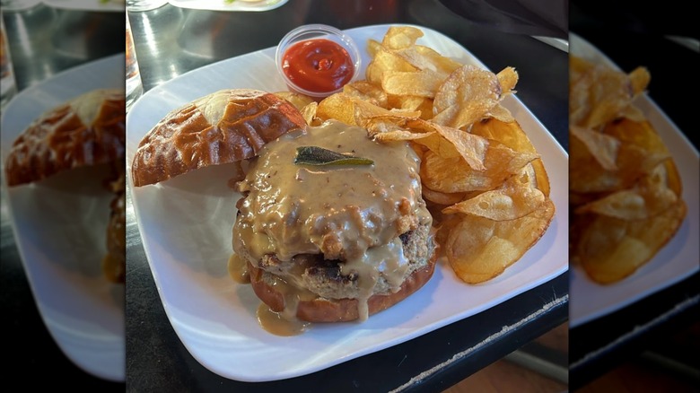 Open burger with potato chips on black restaurant table, mirrored image