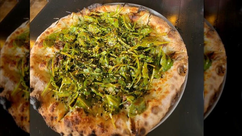 A pizza covered in greens on black restaurant table, mirrored image