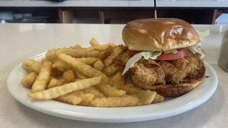 A pork sandwich with crinkle cut fries on white plate on white restaurant table