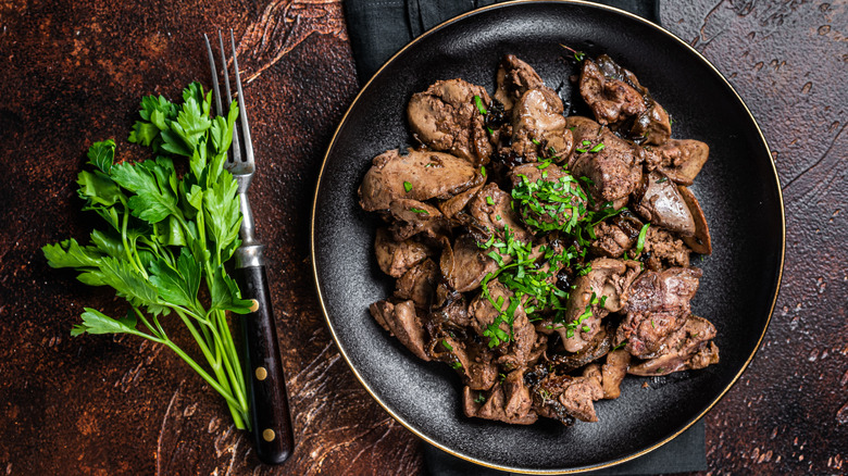 Fried chicken livers on a plate with a sprig of parsley next to it.