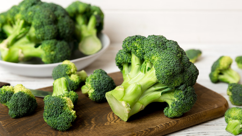 Whole broccoli and florets on a wooden board