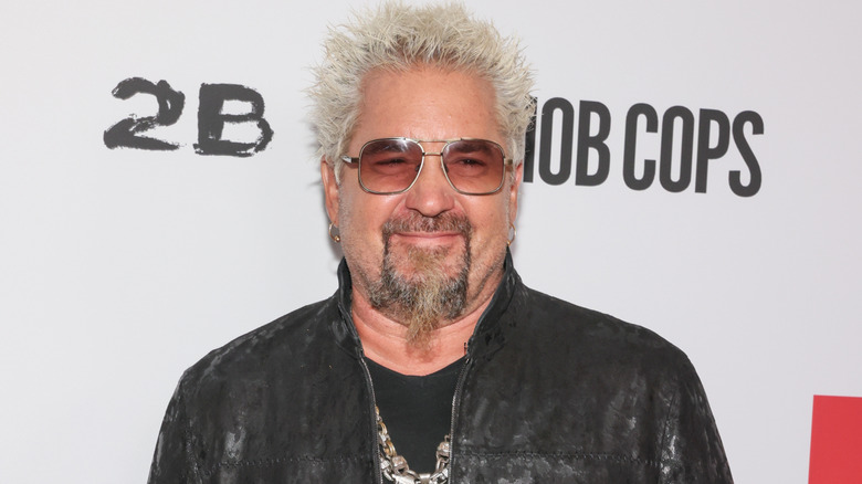 Guy Fieri smiles in black zip-up jacket and sunglasses