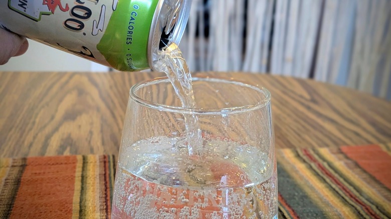 A close-up of sparkling water pouring from a can into a round Waterloo-branded glass