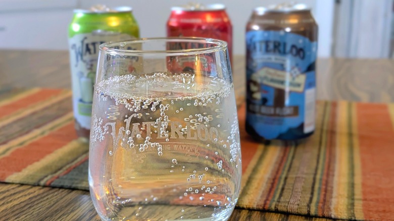Sparkling water in a Waterloo-branded glass with three cans of sparkling water in the background