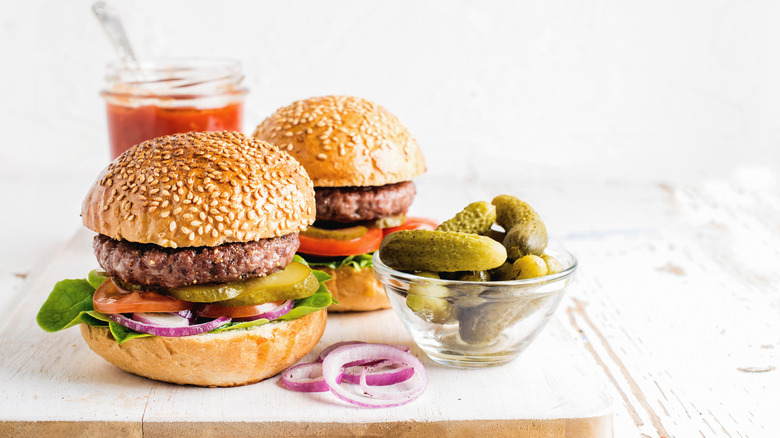 Two burgers on wooden board with side of pickles