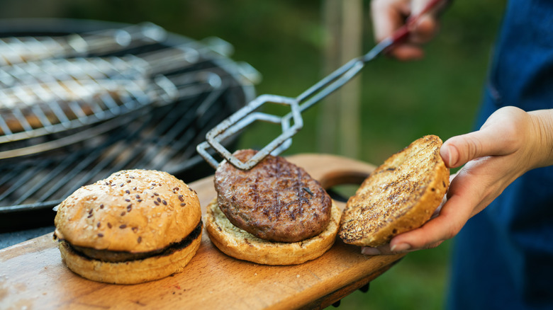 Placing burgers on grilled buns with blurred grill in background