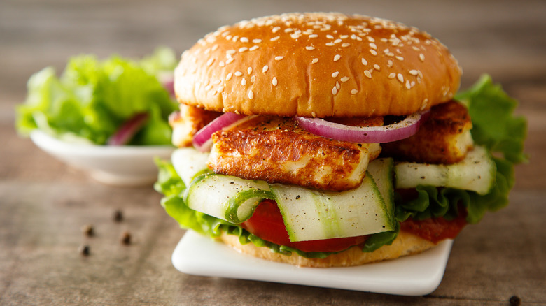 Burger with fried halloumi, onion, lettuce, tomato, and sliced cucumber