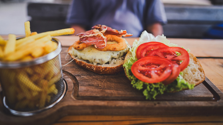Burger open to show onion rungs, bacon, lettuce, and tomato