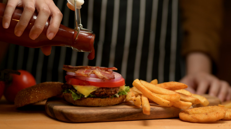 Hand of unidentified person pouring ketchup onto burger