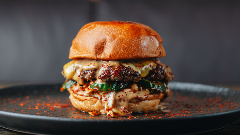 Burger with melty cheese with chili flakes on black plate