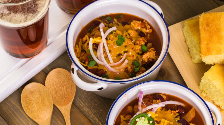 rich dark chili in bowls topped with cheese with beer and cornbread