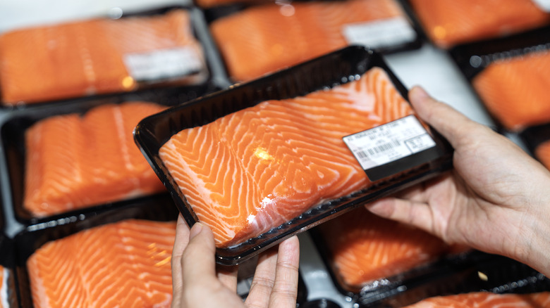 Hands holding a shrink wrapped package of salmon at a grocery store