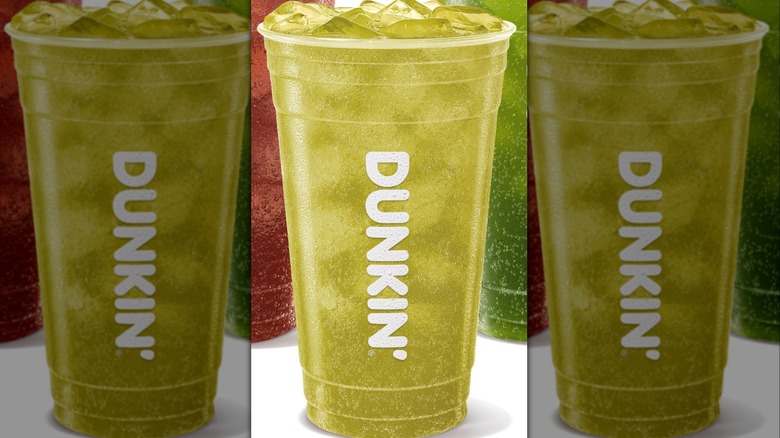A cup of Dunkin's Candy Kiss Dunkin' Zero against a backdrop of two other Dunkin' seasonal drinks