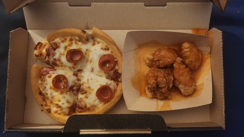 A My Haunt Box features a personal pan pizza with cupped pepperoni and four breaded wings. It sits on a blue countertop