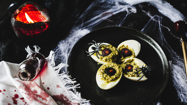 four deviled eggs with plastic spiders on black plate