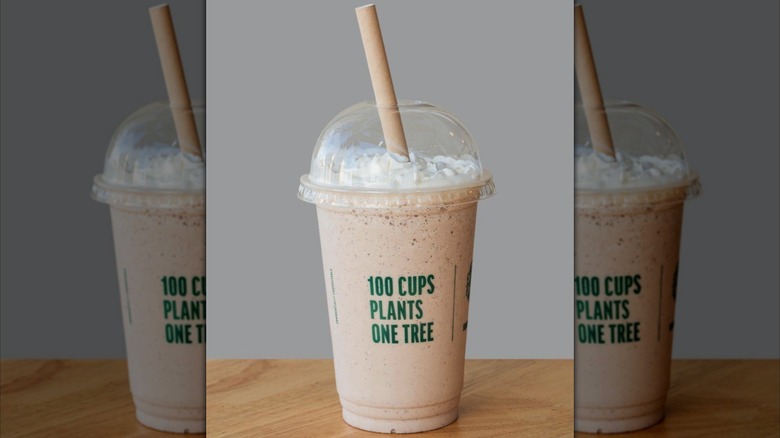 Milkshake topped with whipped cream in clear plastic cup with straw sticking out