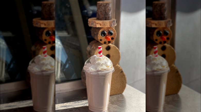 Chocolate milkshake topped with whipped cream in plastic cup in front of decorative wooden snowman
