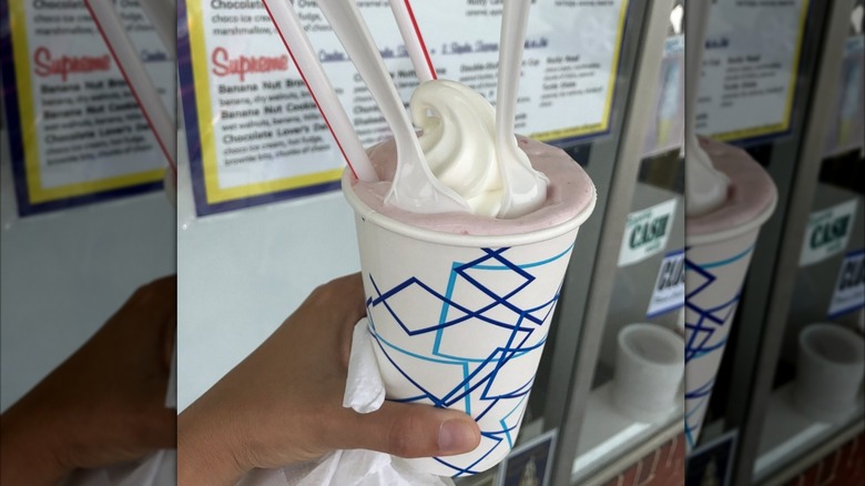 Hand holding milkshake topped with whipped cream in front of menu taped on window