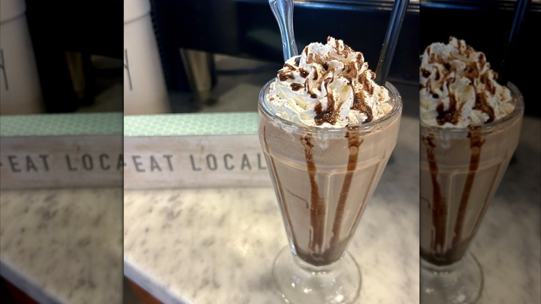 Glass filled with milkshake, topped with whipped cream and chocolate syrup