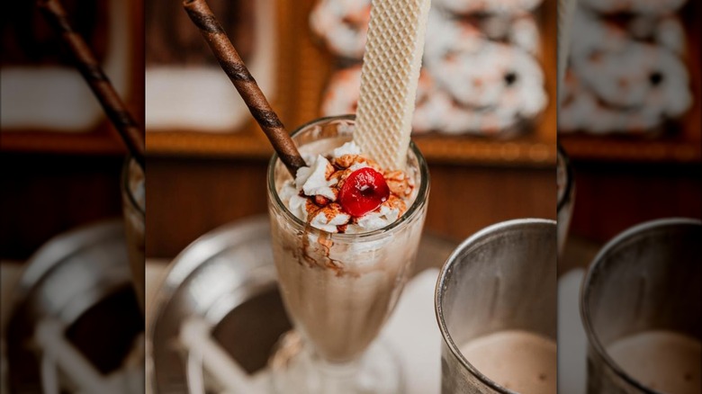 Milkshake in glass topped with wafer, wafer straw, whipped cream, and cherry