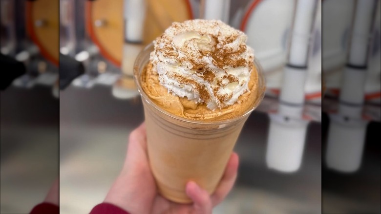 Hand holding pumpkin pie milkshake topped with whipped cream and spice