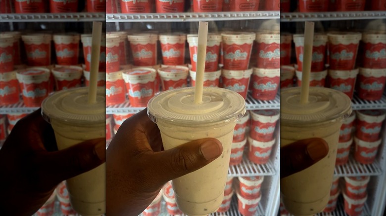 Hand holding cookie dough and brown butter milkshake in front of freezer with ice cream pints