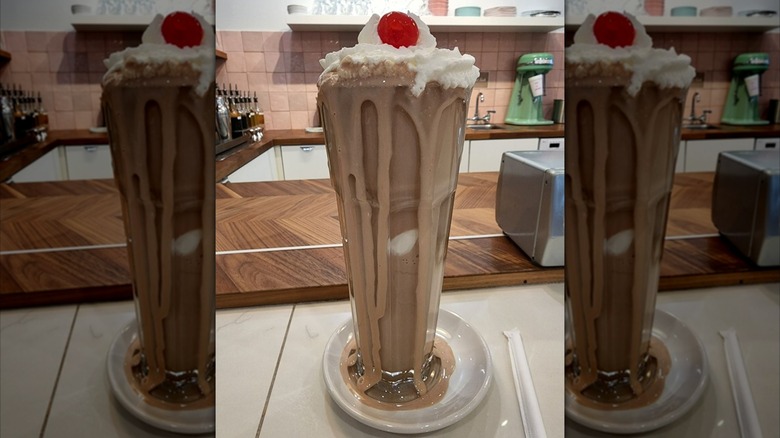 Chocolate malt overflowing from tall glass with whipped cream and cherry on top