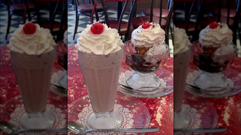 Cookie monster milkshake next to sundae in glass bowl, both topped with whipped cream and cherries