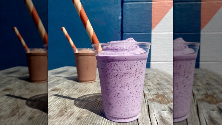 Blueberry buttermilk and chocolate milkshakes on wooden table, both with straws
