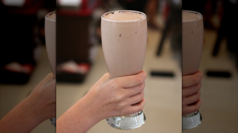 Hand holding milkshake in tall glass