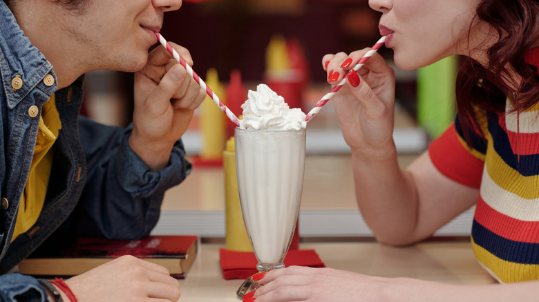 Two people sipping milkshake from glass in classic diner