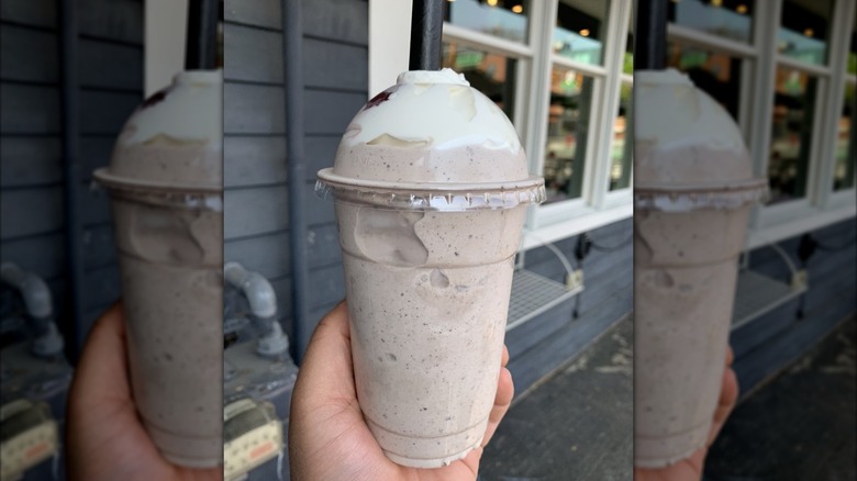 Hand holding cookies and cream milkshake on sidewalk