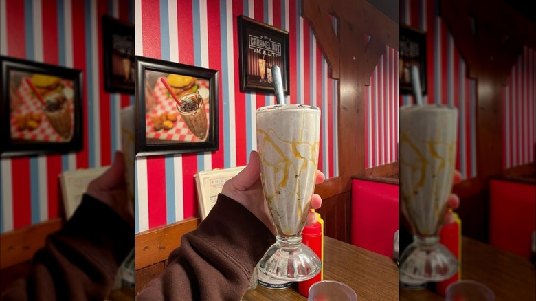 Hand holding vanilla malt with butterscotch and Oreo in diner