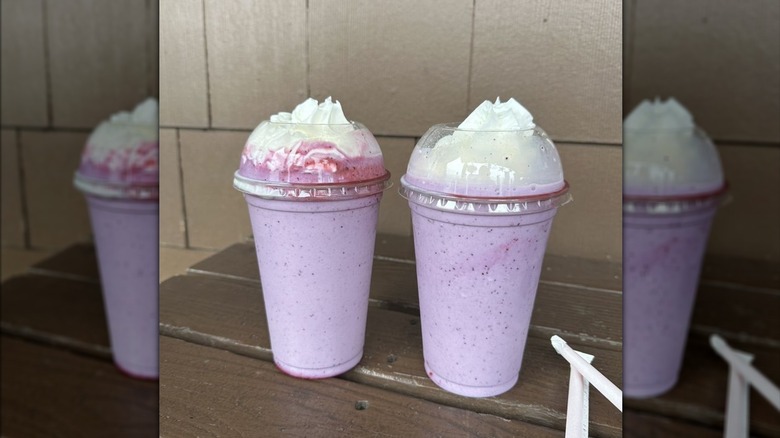 Two huckleberry milkshakes topped with whipped cream on table