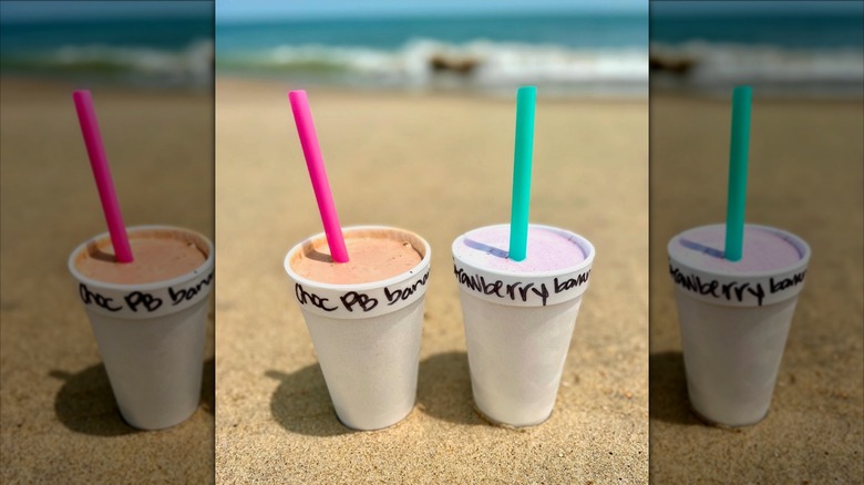 Chocolate peanut butter banana and strawberry banana milkshakes on beach with ocean in background