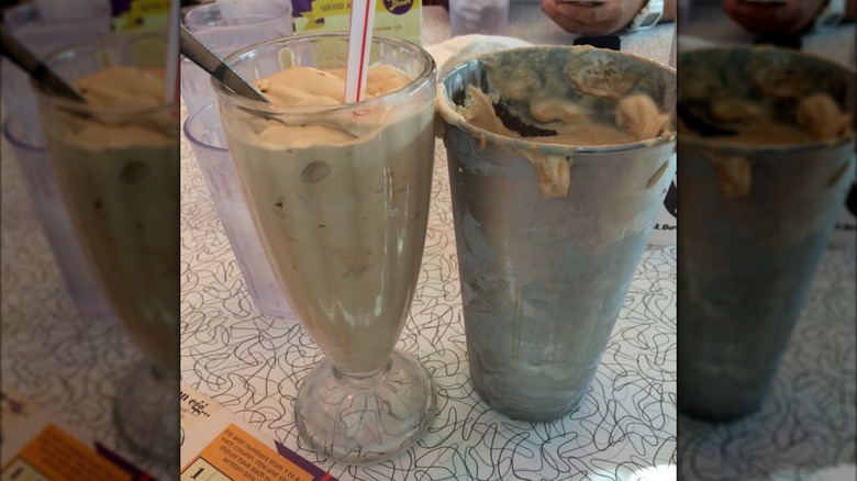 Peanut butter chocolate milkshake in glass next to metallic container with extra shake