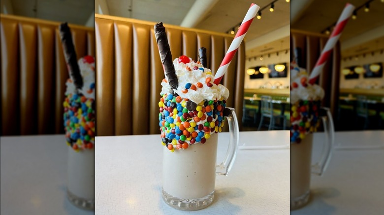 Milkshake adorned with chocolate candies, whipped cream, chocolate wafer straws, and cherry