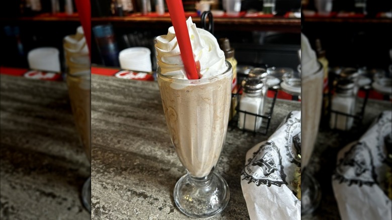 Oreo milkshake in glass topped with whipped cream on counter