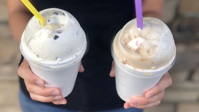 Hands holding chocolate shake and banana chocolate chip cookie dough shake