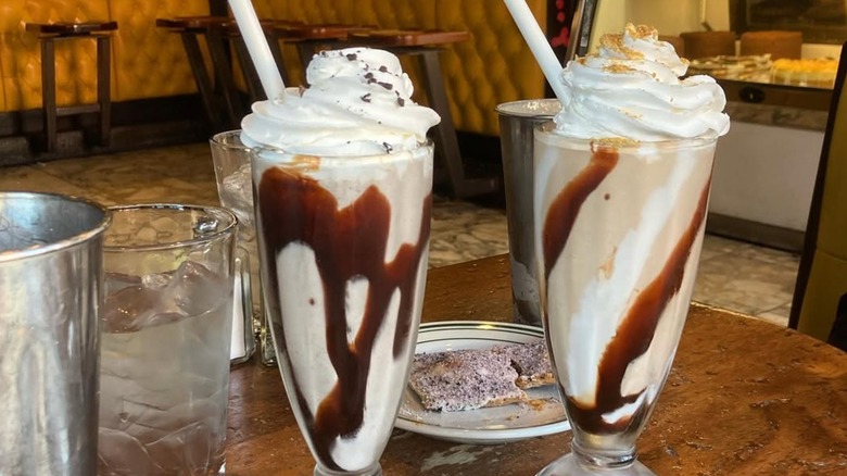 S'mores milkshake and peppermint junior milkshake in glasses, topped with whipped cream and decorated with hot fudge