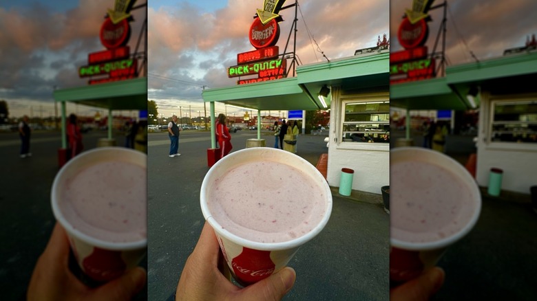 Hand holding strawberry malt shake in Pick Quick parking lot
