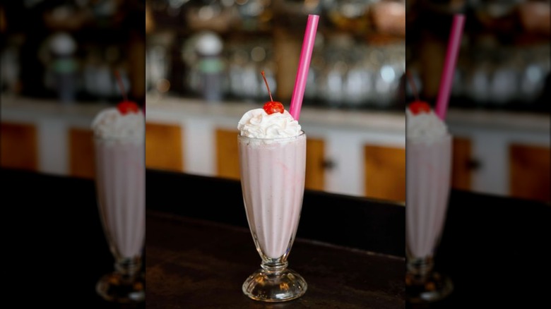 Milkshake in tall glass topped with whipped cream and cherry