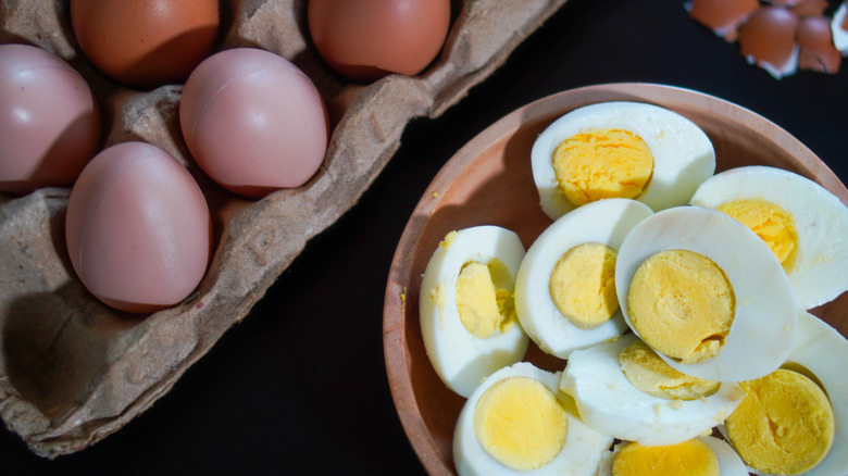 Bowl of halved hard-boiled eggs next to a carton of eggs in the shell