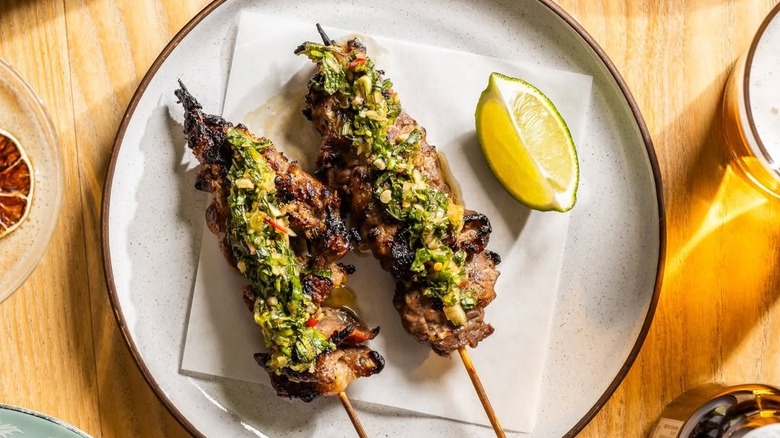 Two plated beef skewers and a lemon wedge on a napkin